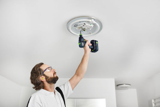 Festool TXS 18 Akku-Bohrschrauber bei Deckeninstallation mit Batterie in der Hand