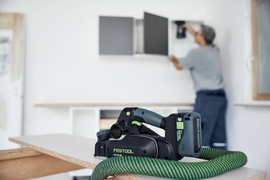 Festool HLC 82 GB Elektro-Hobel mit Akkupacks BP 18 Li und TCL 6 DUO Ladegerät auf Werkbank, Anwendung im Hintergrund