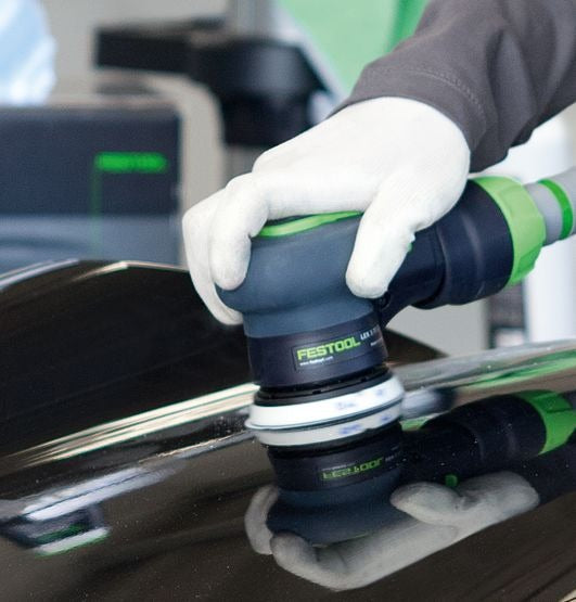 Festool Schleifteller ST D77-M5-W mit Klettbelag wird an schwarzer Oberfläche angewendet, Hände mit Schutzhandschuhen