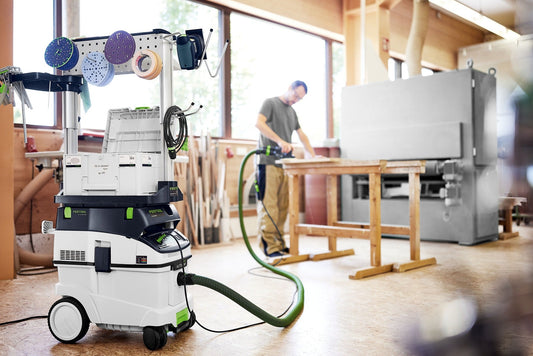 Festool CLEANTEC CTM 36 EI AC Absaugmobil mit Zubehör an Werkstatt-Stele, Handwerk in Werkstatt im Hintergrund.