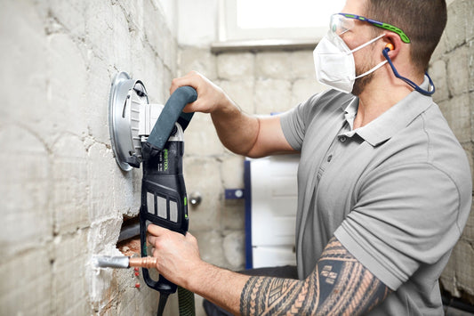 Festool Sanierungsschleifers RG 130 mit Führungstisch GT-RG 130 beim Schleifen von Betonwand, Staubabsaugung sichtbar.